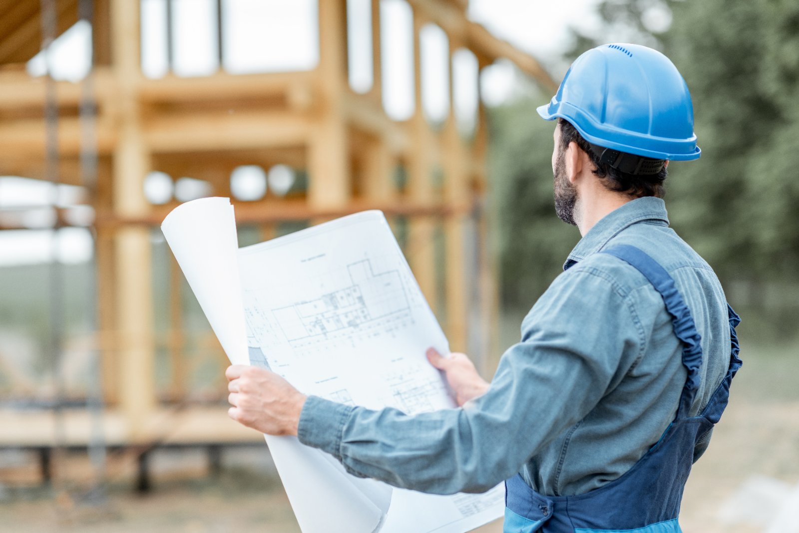 Owner builder in hard hat with plans at a house construction site