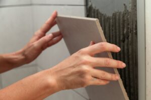 Tiler applying adhesive and placing a ceramic wall tile during a bathroom renovation